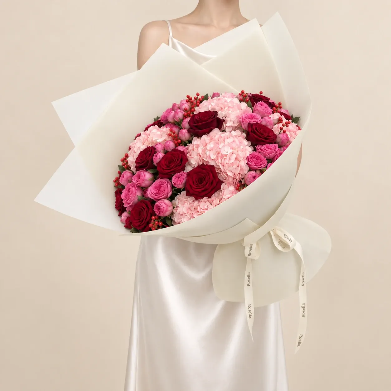 A generous bouquet of red roses, pink spray roses, blush hydrangeas and red berries, wrapped in ivory paper and tied with a Rosella ribbon