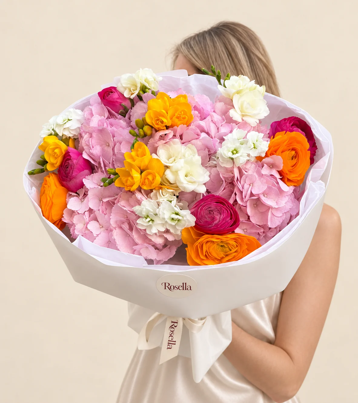 4 hydrangeas, 4 pink ranunculus, 3 orange ranunculus, 3 yellow freesias, 1 stock & 2 cream freesias in a hand-tied bouquet