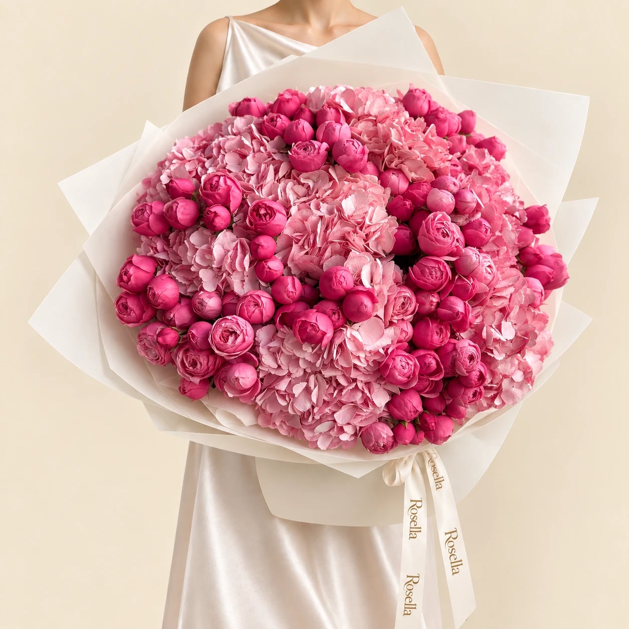 A huge dome of bright pink peony buds over soft pink hydrangeas in wide ivory wrap tied with a Rosella ribbon, held by a woman in a champagne satin dress