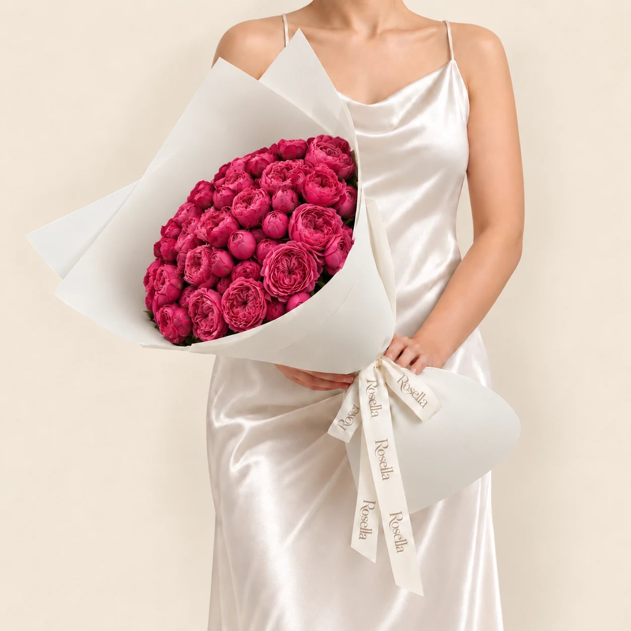 A bouquet of 60 raspberry pink Juliet spray roses wrapped in ivory paper and tied with a Rosella ribbon, held by a woman in a champagne satin dress