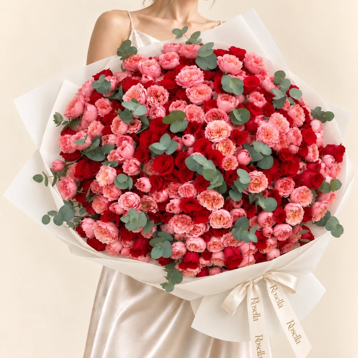 A huge dome of about 200 red roses and pink spray roses with sprigs of eucalyptus in wide ivory wrap tied with a Rosella ribbon, held by a woman in a champagne satin dress