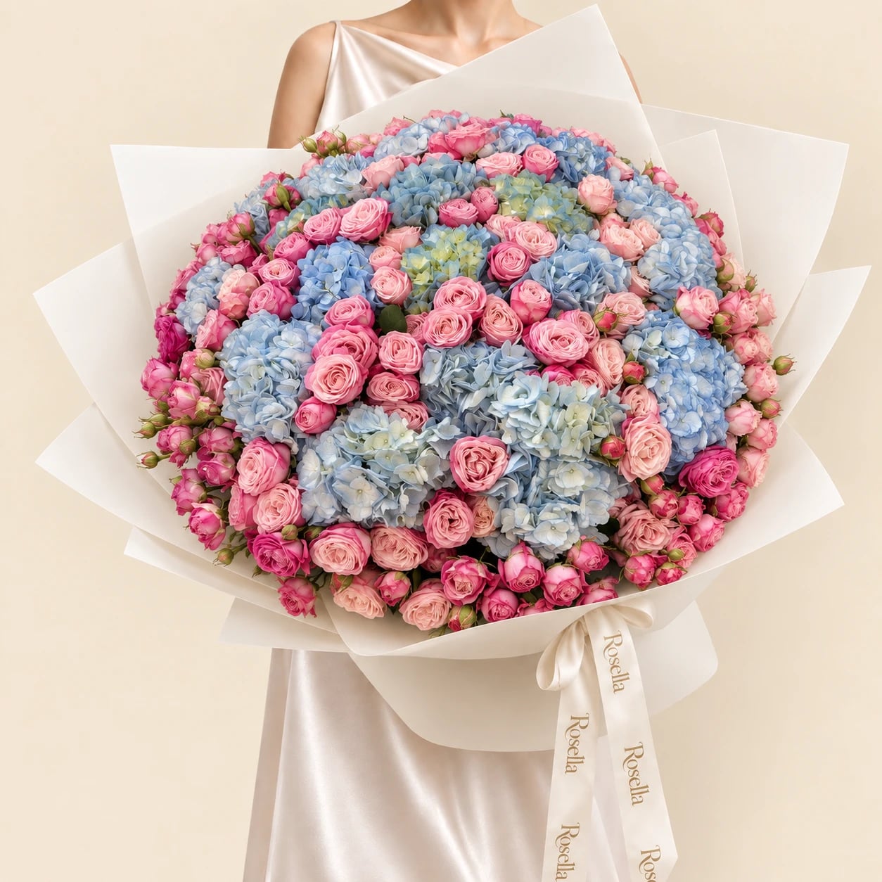 A huge dome of pale blue and green hydrangeas ringed and threaded with pink spray roses in wide ivory wrap tied with a Rosella ribbon, held by a woman in a champagne satin dress